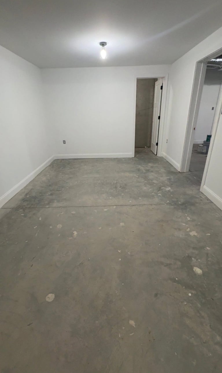 Empty room with white walls, concrete floor, ceiling light, and open doorways leading to other rooms