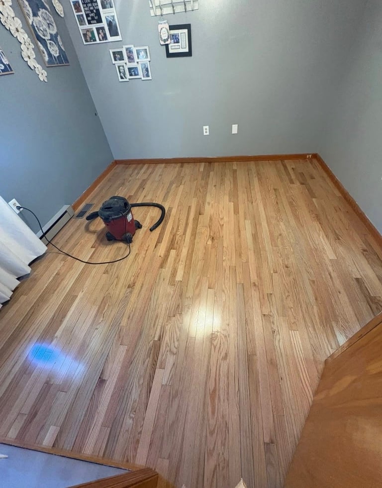 Empty room with blue-gray walls, wood laminate flooring, and a red shop vacuum with hose on the floor