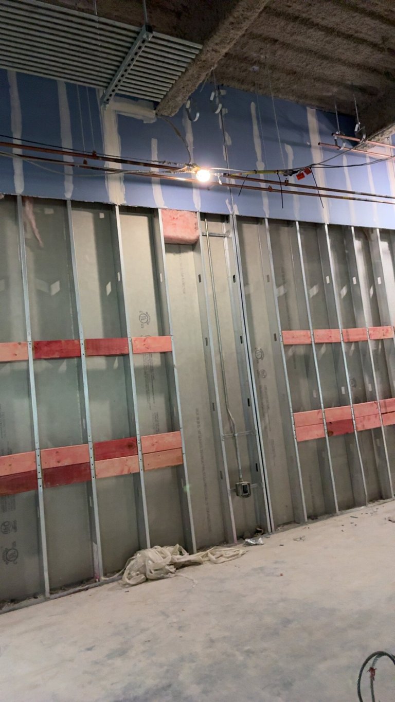 Unfinished warehouse interior with metal-framed glass partition walls featuring red and gray panels and industrial ceiling structure