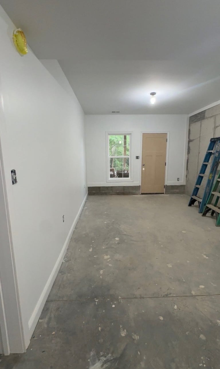 Unfinished interior room with white drywall, concrete floor, window, door, and blue ladder against the wall