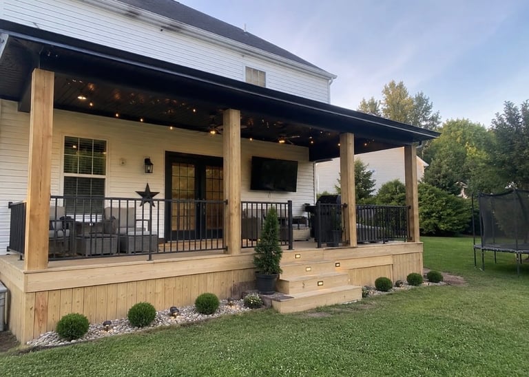 Modern house with wooden porch, black railings, and manicured lawn surrounded by trees