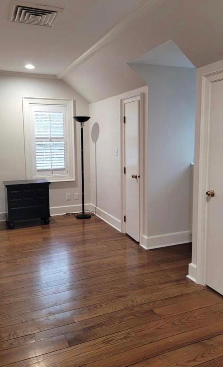 Empty attic room with white walls, wooden floors, angled ceiling, built-in shelving, and multiple doors