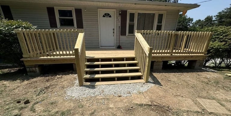 Front view of a beige house with wooden deck and stairs, dual railings, and gravel foundation