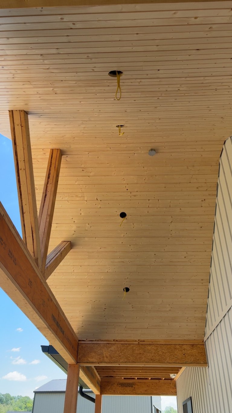 Interior view of wooden ceiling with exposed beams and electrical outlet holes in a covered porch or carport structure