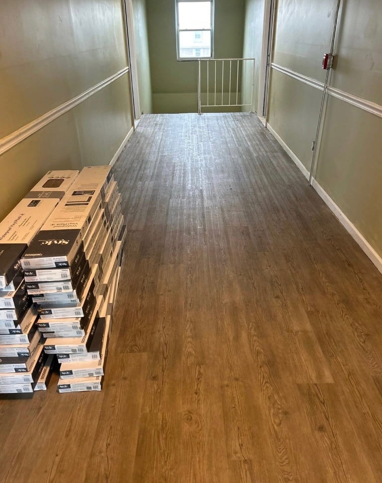 Empty room with wooden flooring, stacked boxes on left side, green walls, and window at far end