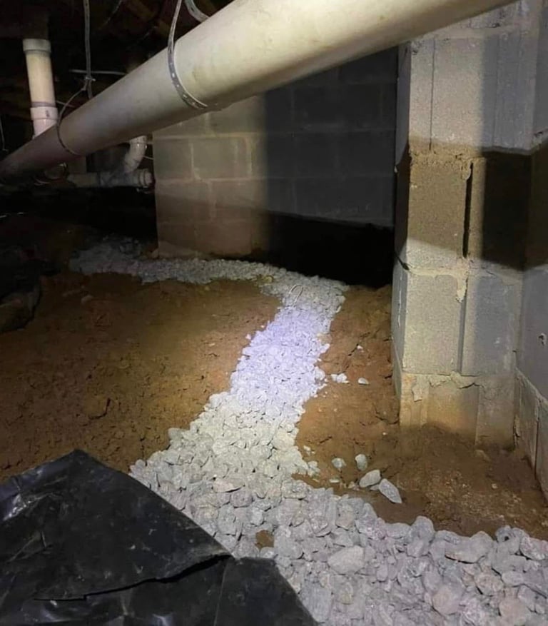 Basement crawlspace with white granular material piled on dirt floor near concrete block wall and metal ductwork pipe above