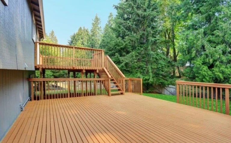 Large wooden deck with multi-level stairs and railings overlooking dense green forest on sunny day