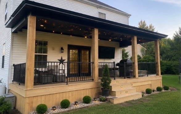 Modern covered porch with wooden posts, black railings, and landscaping on a residential home