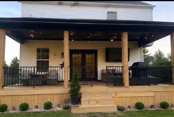 Modern farmhouse exterior with covered porch, black metal railings, wooden columns, and landscaped entry